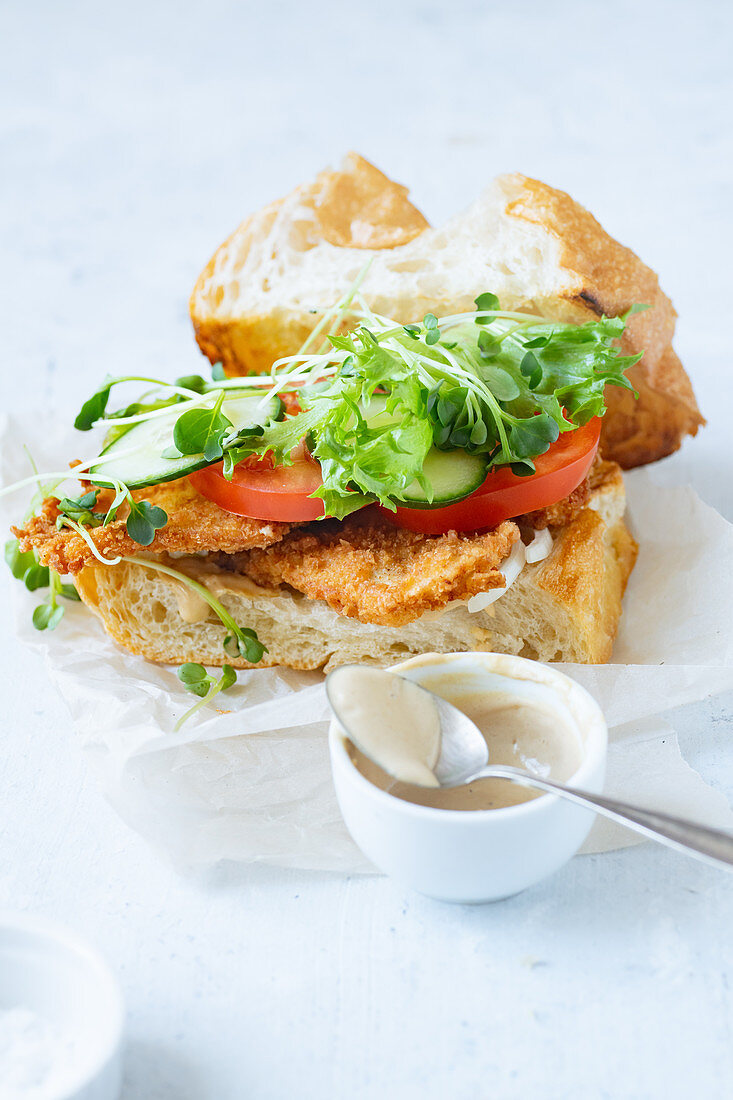Sandwich with fried chicken on chiabatta with tomatoes, cheddar cheese, cucumber, onion, salad and microgreens