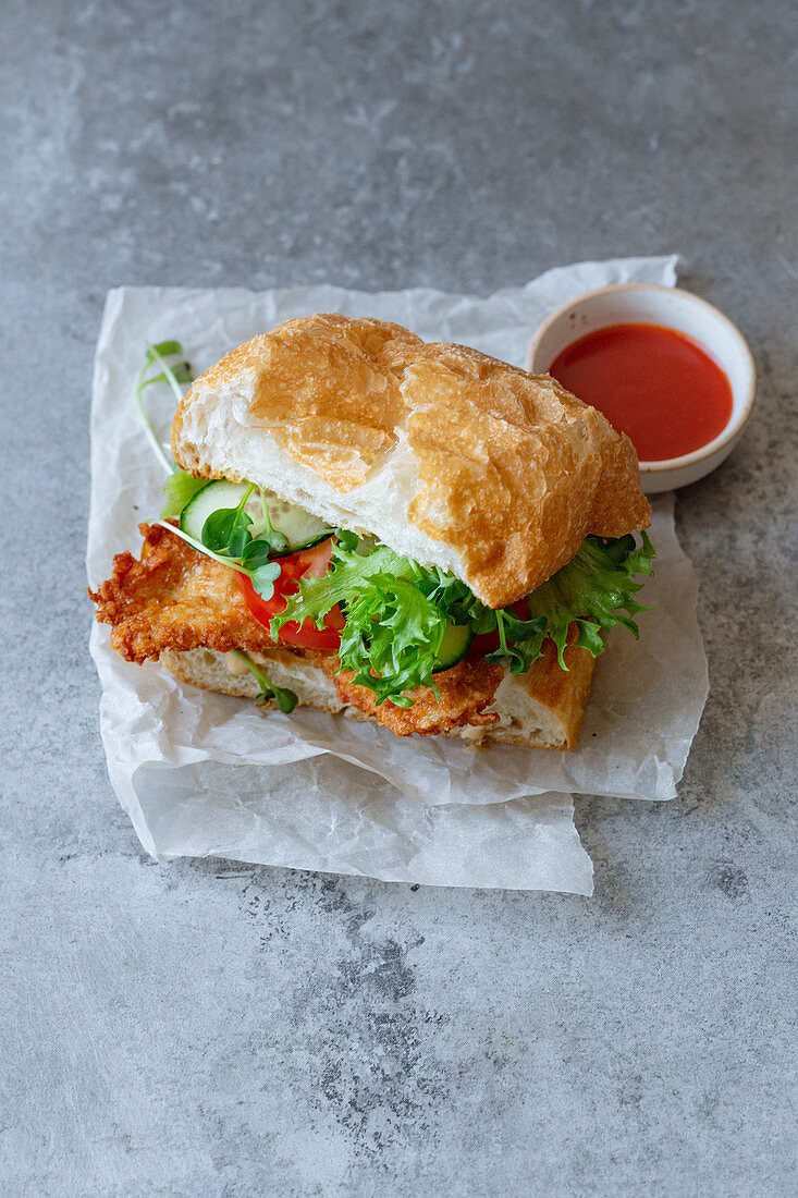 Sandwich with fried chicken on chiabatta with tomatoes, cheddar cheese, cucumber, onion, salad and microgreens