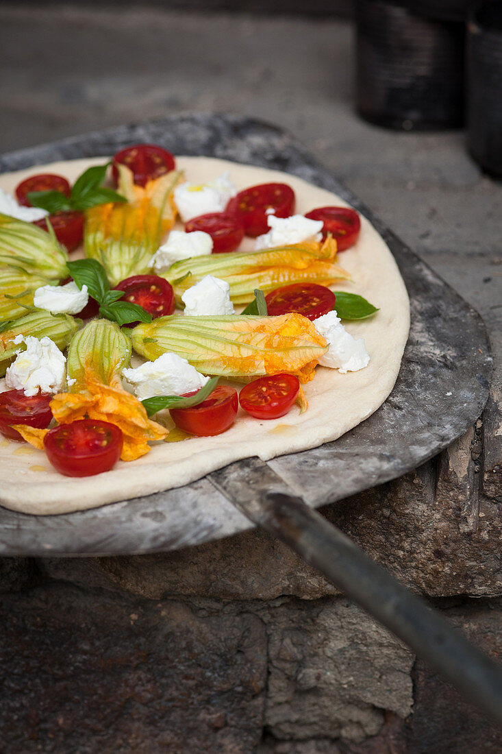 Ungebackene Pizza mit Tomaten, Zucchiniblüten, Mozzarella und Basilikum