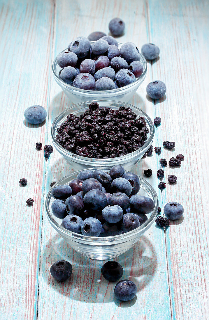 Blueberries (fresh, dried and frozen) in glass bowls