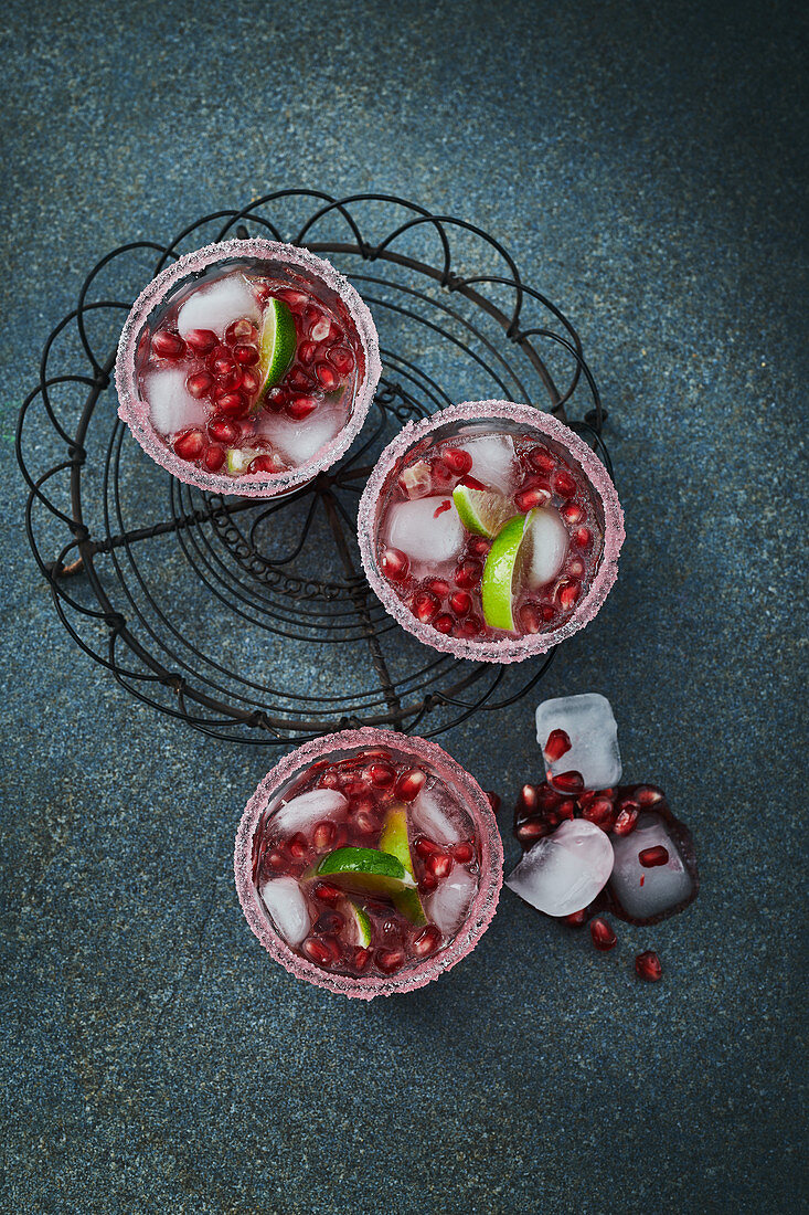 Gin and Tonic with pomegranate seeds in glasses with sugared rims, ice and limes