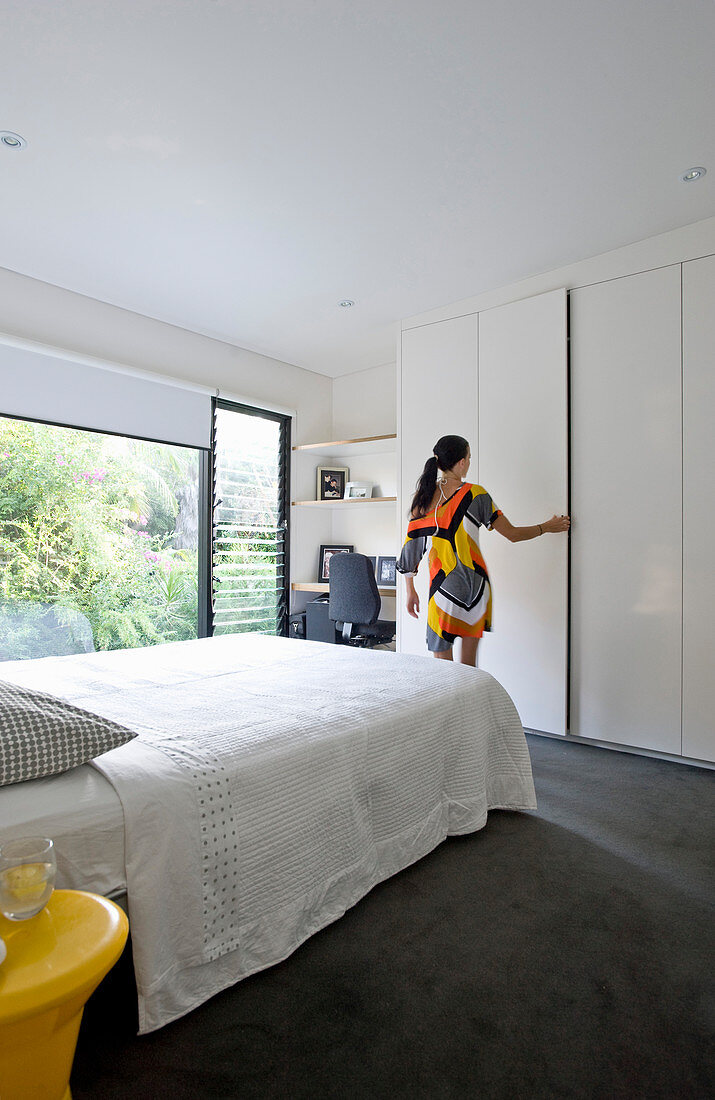 Woman wearing colourful dress stood next to wardrobe in bedroom