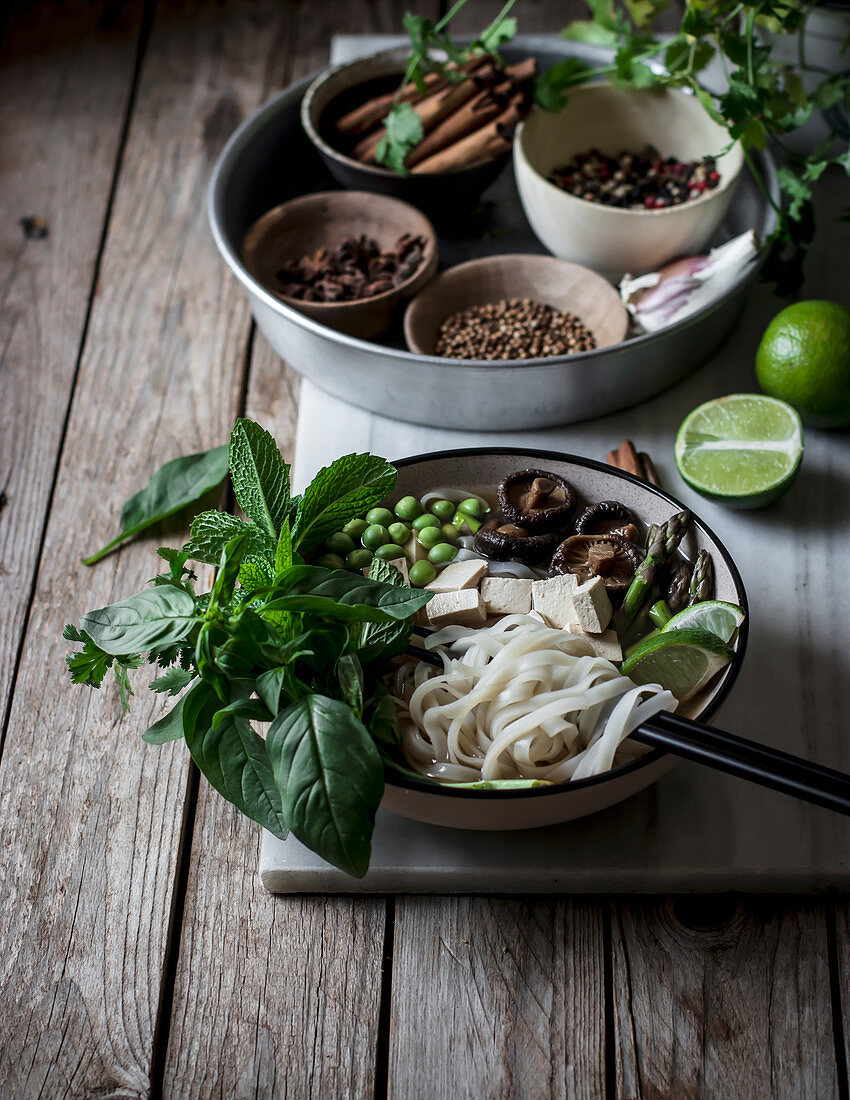 From above of arranged bowls with dry spices and served Pho soup with noodles on marble board