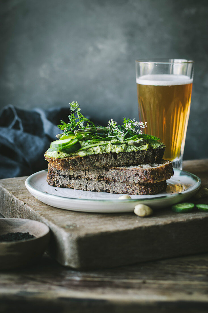 Toast mit grüner Cashewpaste und Gurkenscheiben auf Holzbrett