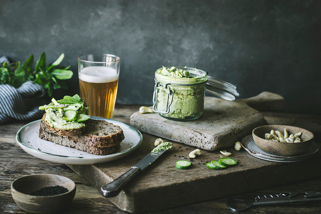Toasts with green cashew pate and slices of cucumber on wooden board