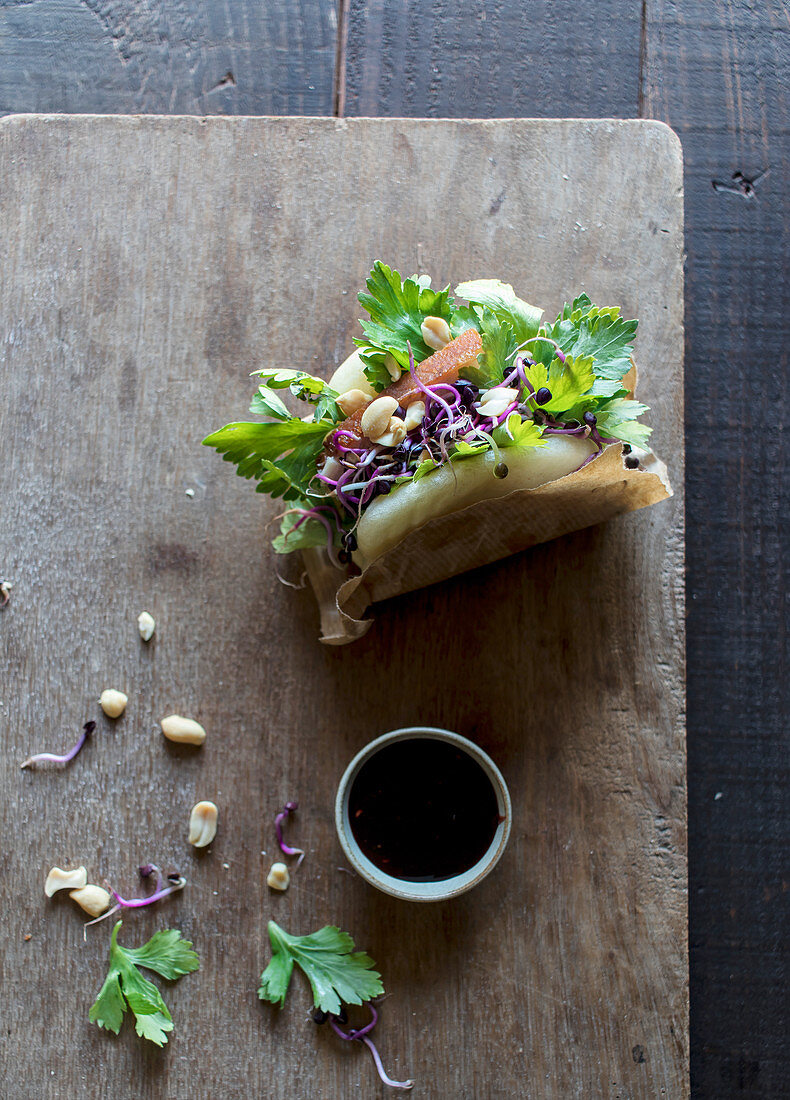 From above of delicious traditional Gua Bao sandwich with parsley and grain sprouts served on board with sauce