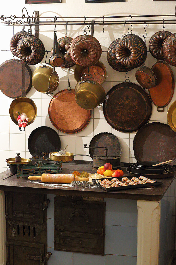 Biscuits and baking ingredients on old wood-fired stove below vintage pans and cake tins on wall in kitchen