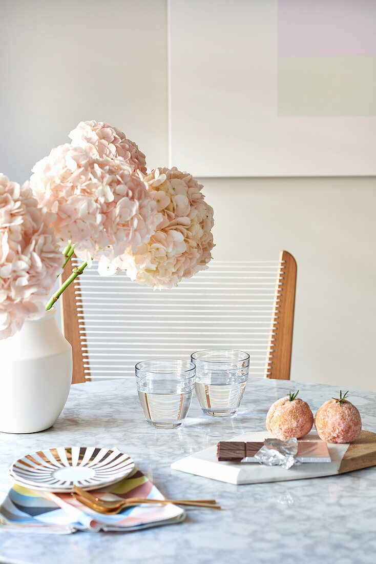 Pink flowers and glasses of water on marble breakfast table and pastries on board