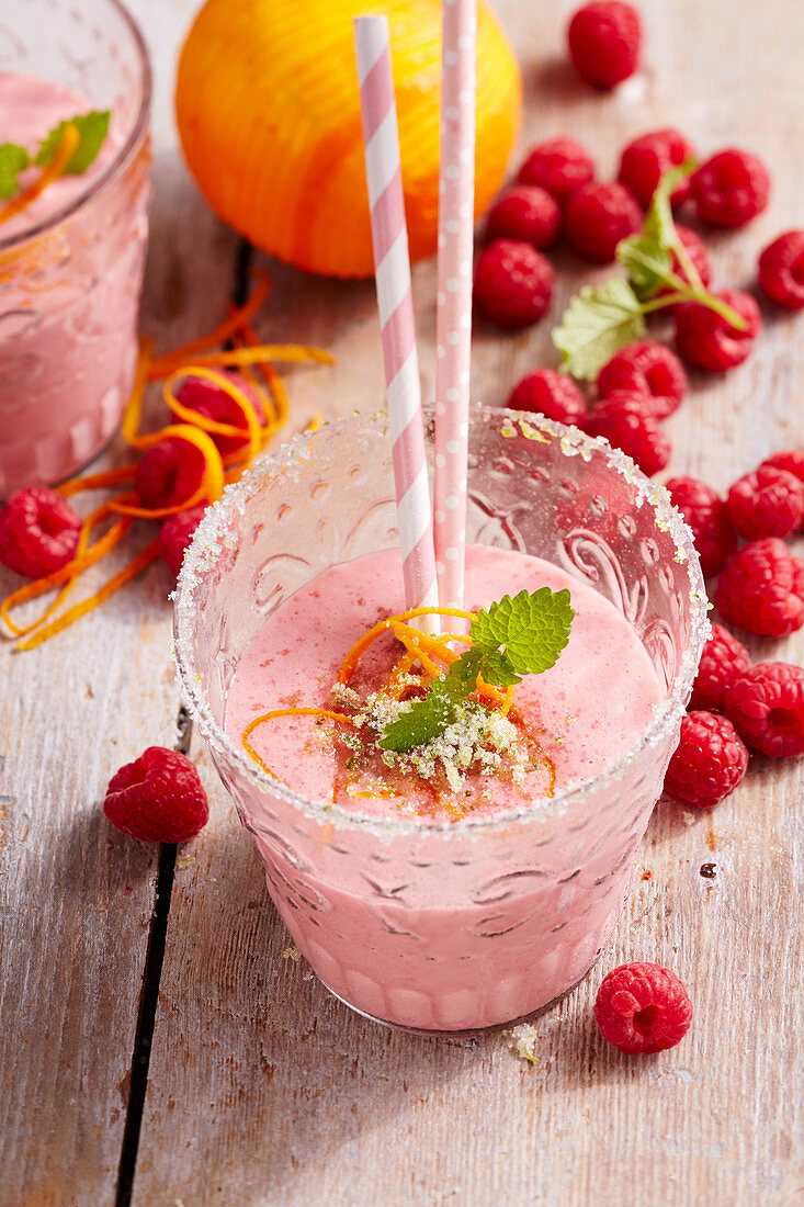 Raspberry and orange milkshakes in glasses with fresh berries and straws
