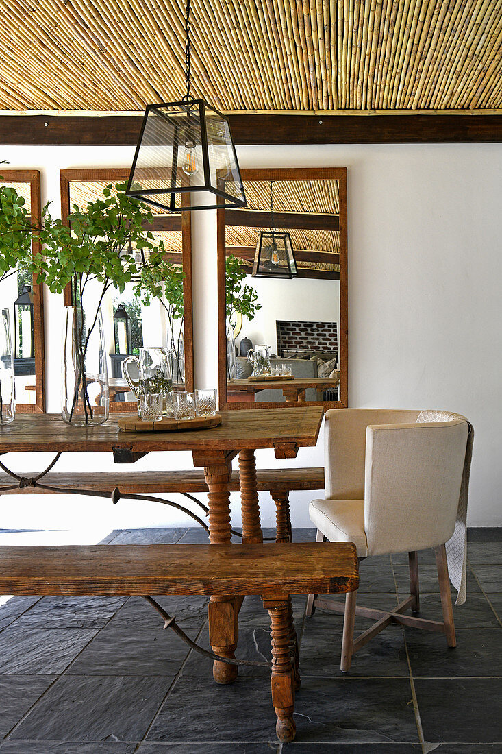 Rustic wooden table with benches and armchair on roofed terrace