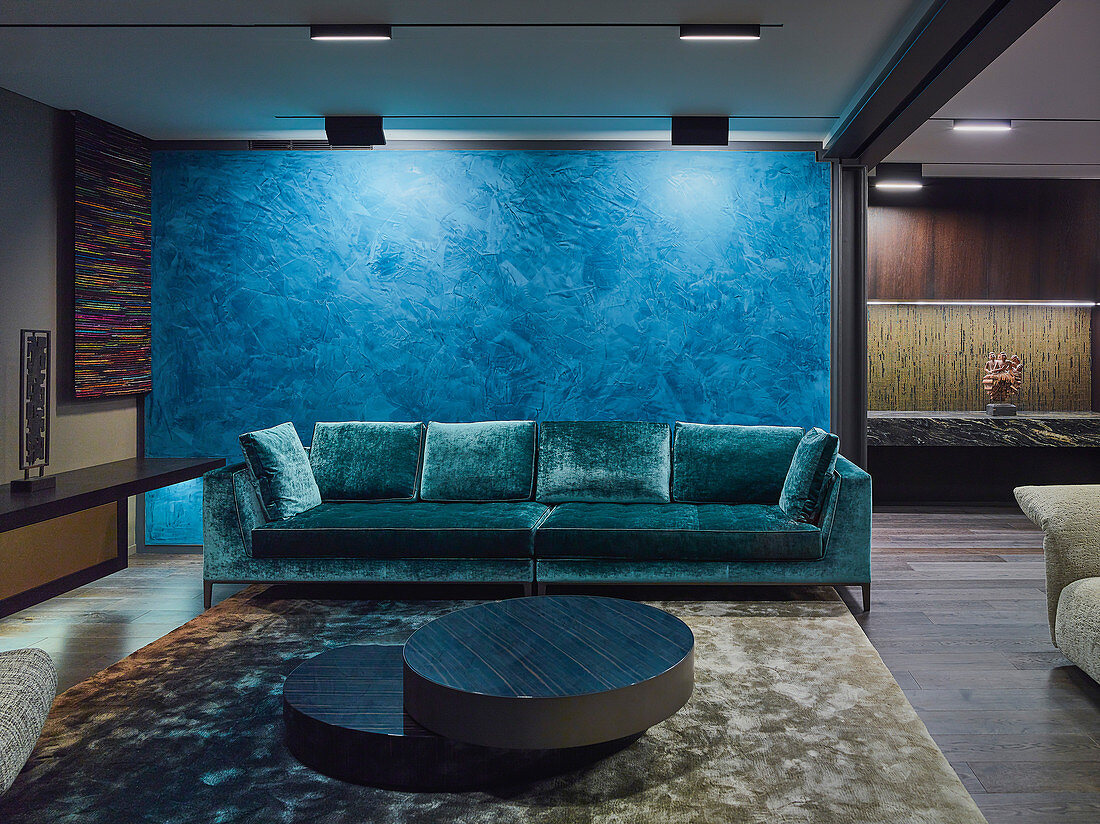 Elegante Lounge mit Designer-Sofas vor blauem Raumteiler in offenem Wohnraum