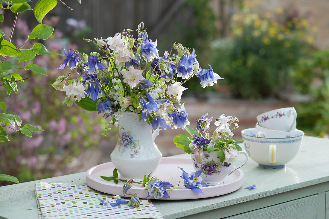 Small spring bouquets of columbine and lily of the valley in cream jugs