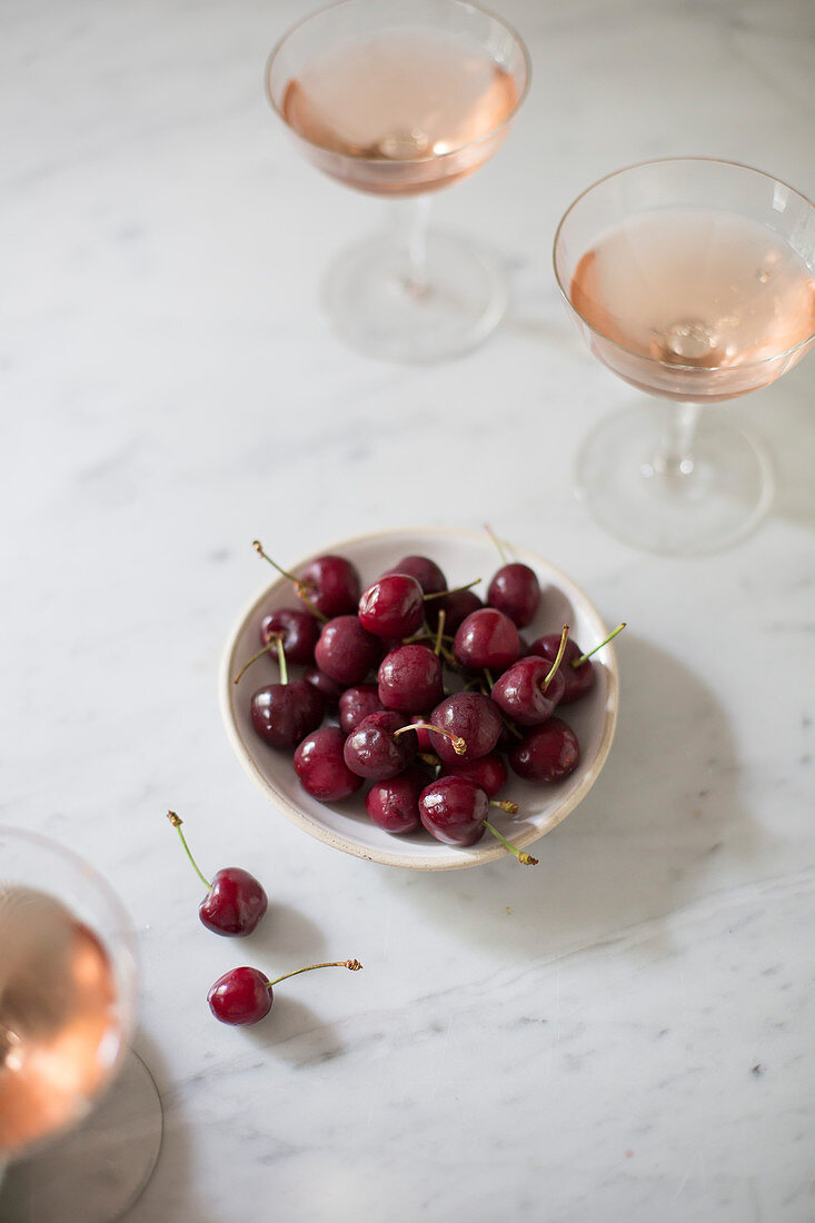 A bowl of cherries next to glasses of champagne
