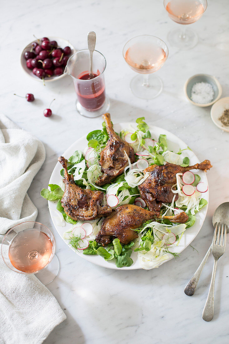 Duck legs on a bed of salad served with cherry sauce and champagne
