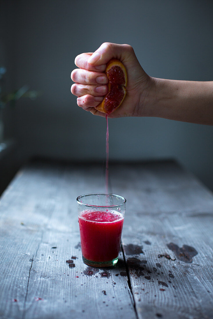 Blood orange juice being pressed into a glass by hand