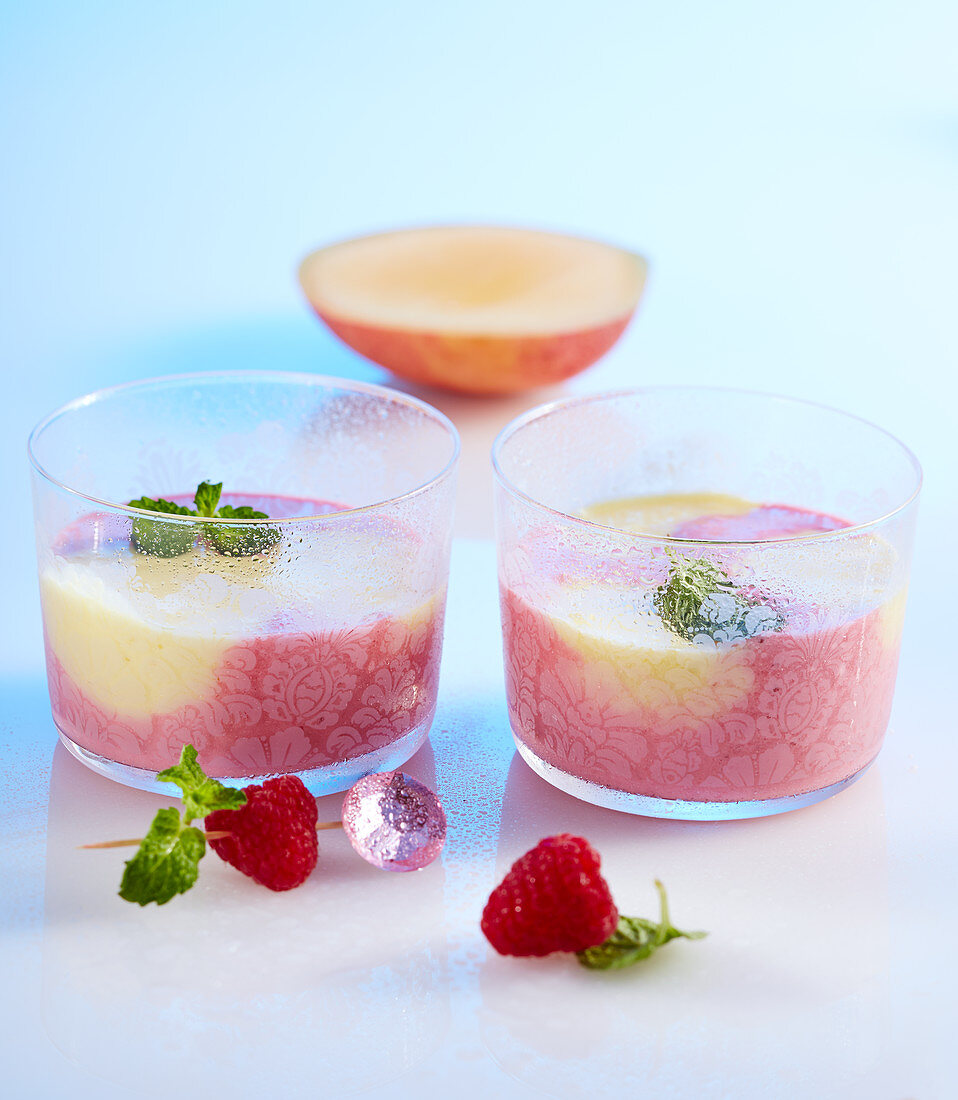 Raspberry and mango smoothie in two small glasses with yoghurt, milk and lemon balm