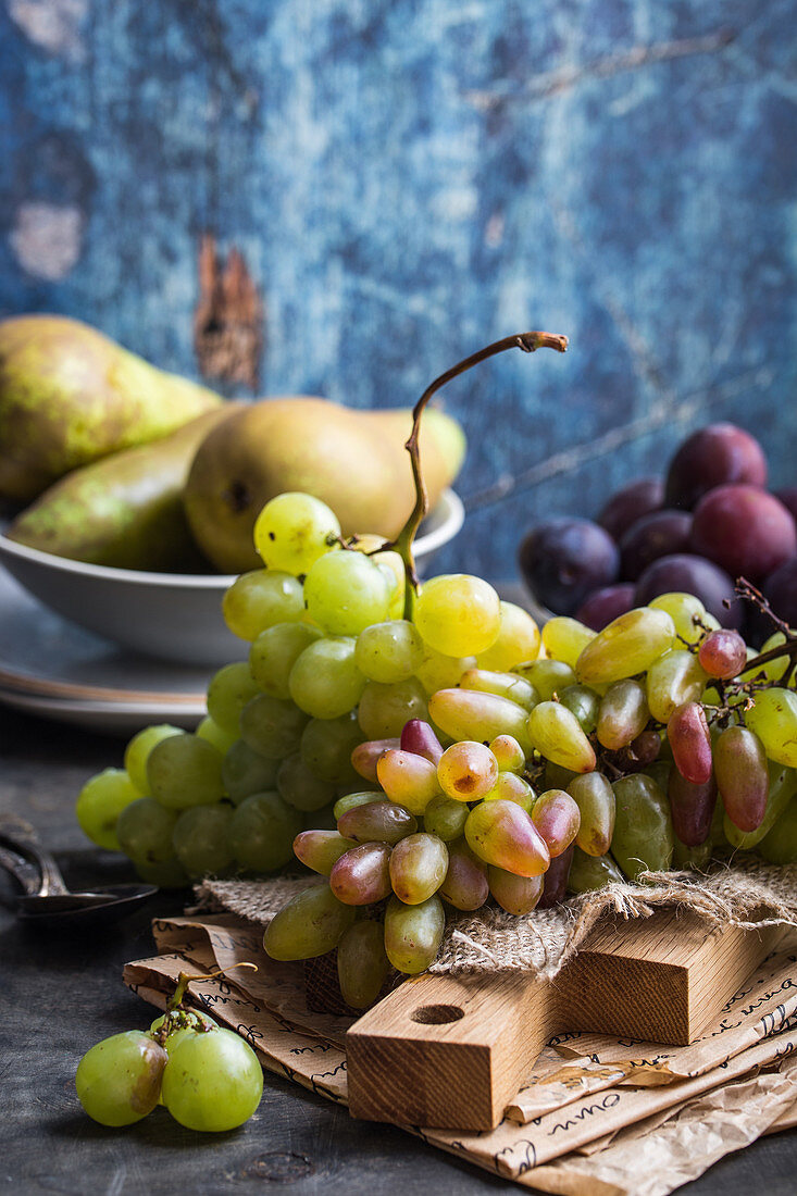 Fresh ripe grapes on wooden cutting board, pears and plums in bowls, wooden rustic background