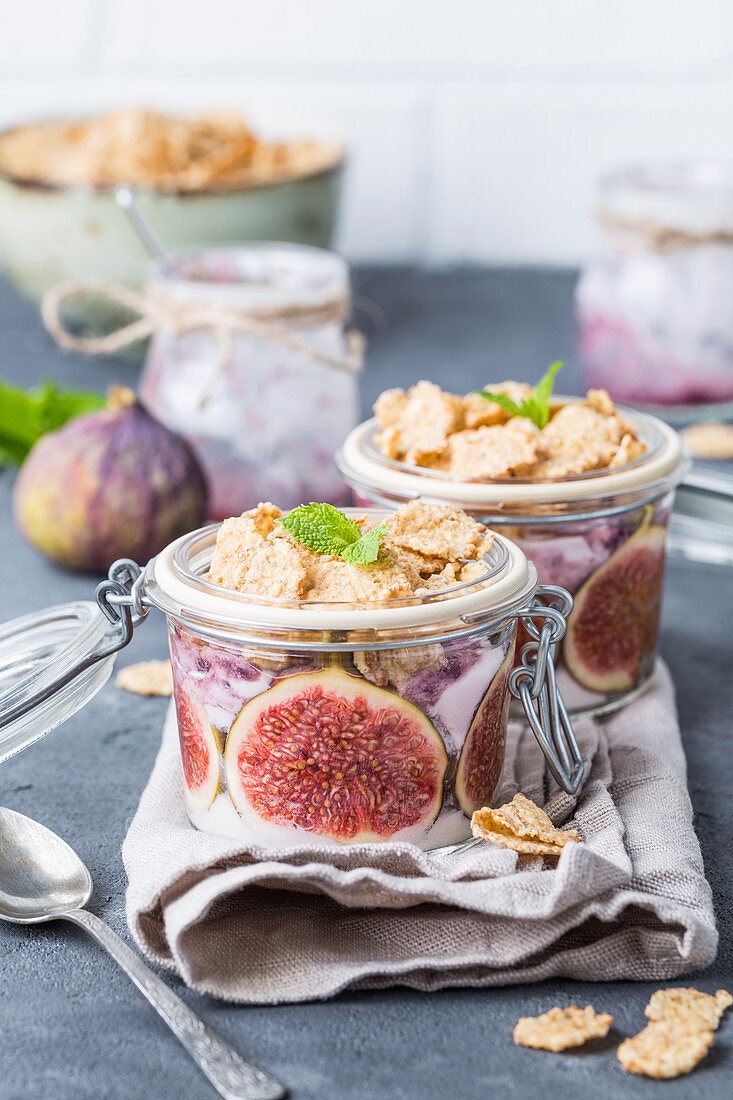 Homemade healthy yoghurt in glass pot with cereals, figs, mint on rustic concrete background