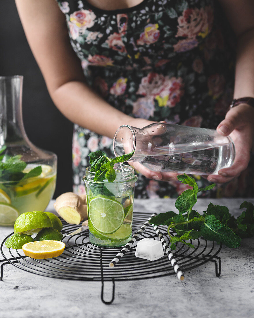 Infused water with lemon, lime, ginger and mint. woman pouring water