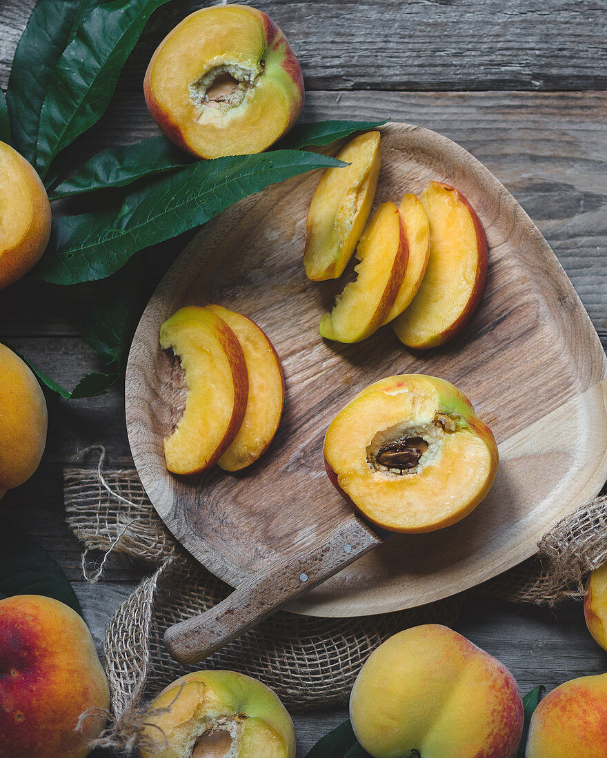 Wooden plate with peaches. peaches with leaves, wooden knife cutting peaches