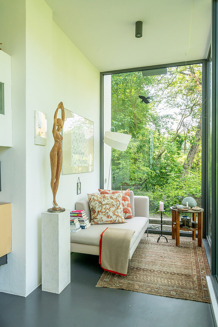 Statue of woman on plinth and couch next to glass wall