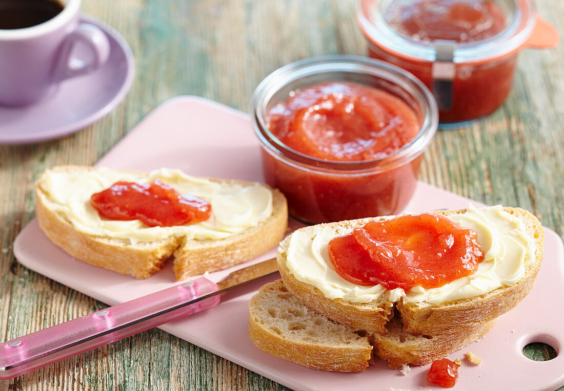 Strawberry and banana jam in jars and on slices of buttered bread