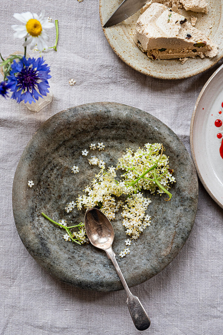 Elderflower in a stone bowl next to halva on a dessert plate