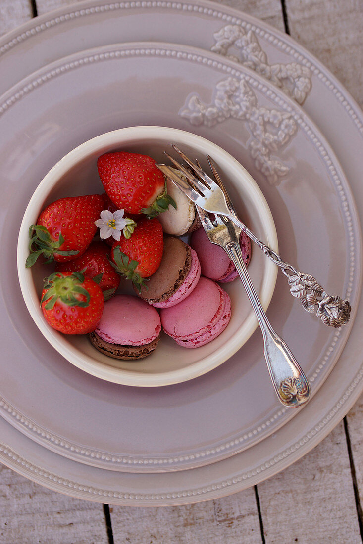 Verschiedene Macarons und frische Erdbeeren in Schälchen auf Tischgedeck