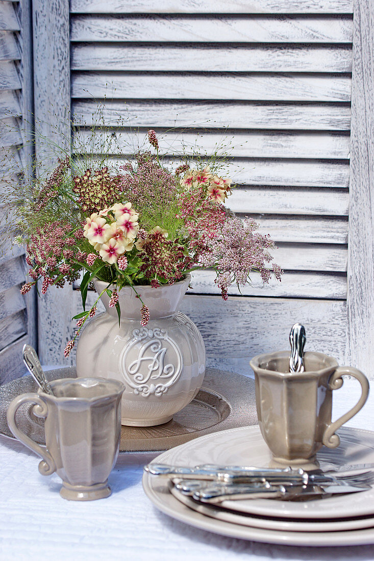 Bouquet of wild carrot flowers in vase next to grey crockery