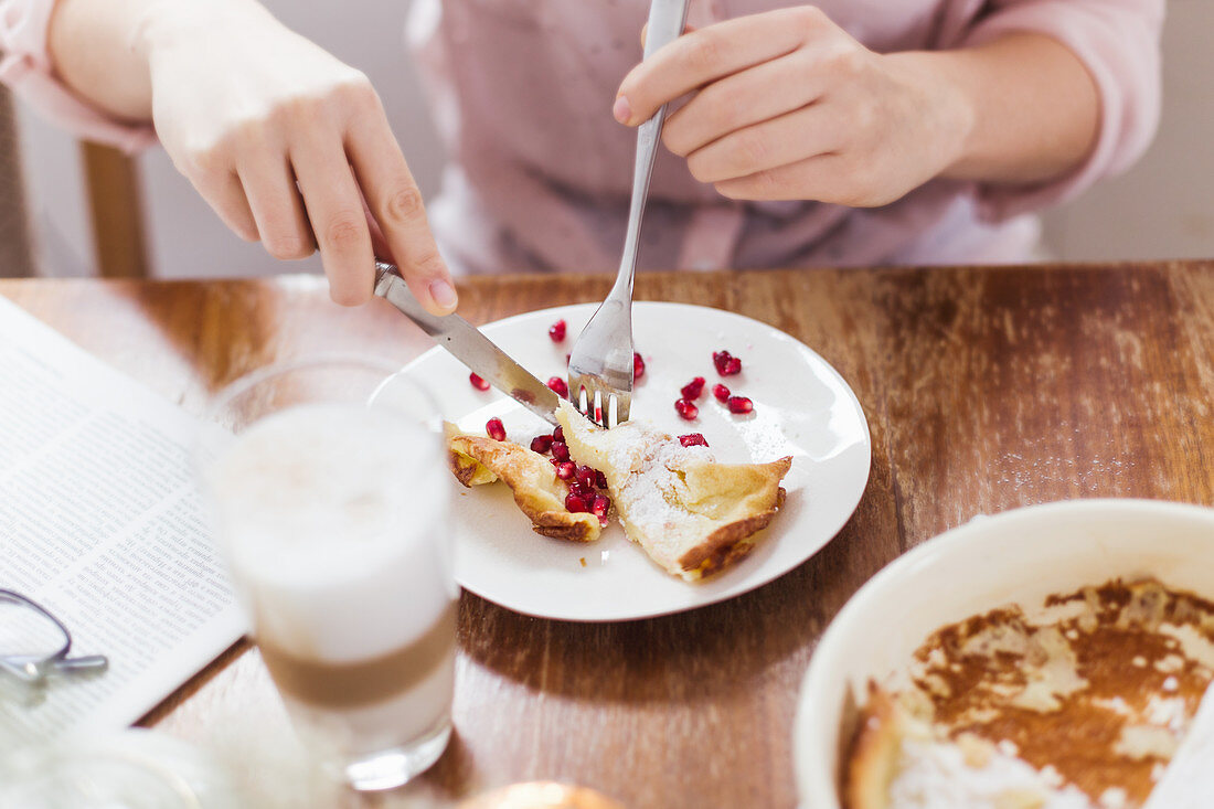 A woman eating oven-baked pancakes with pomegranate seeds