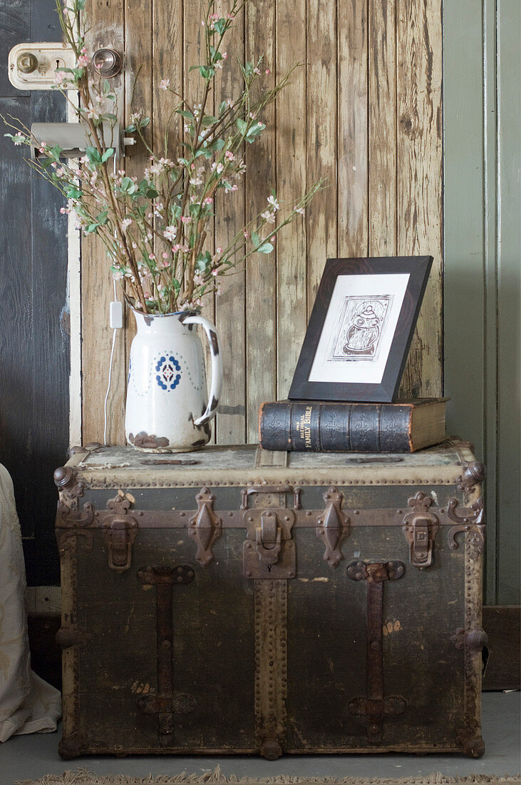 Flowering branches in jug, book and drawing on old steamer trunk