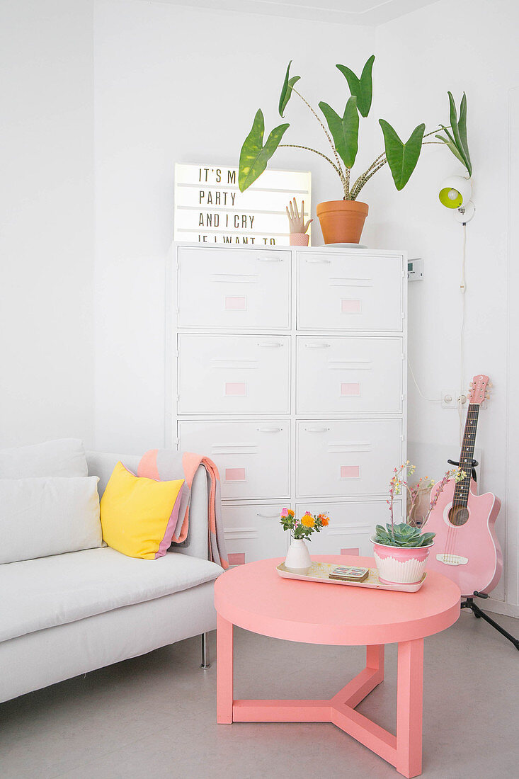 Sofa und Metall-Hochschrank in Weiß mit rosa Farbakzenten durch Couchtisch und Gitarre