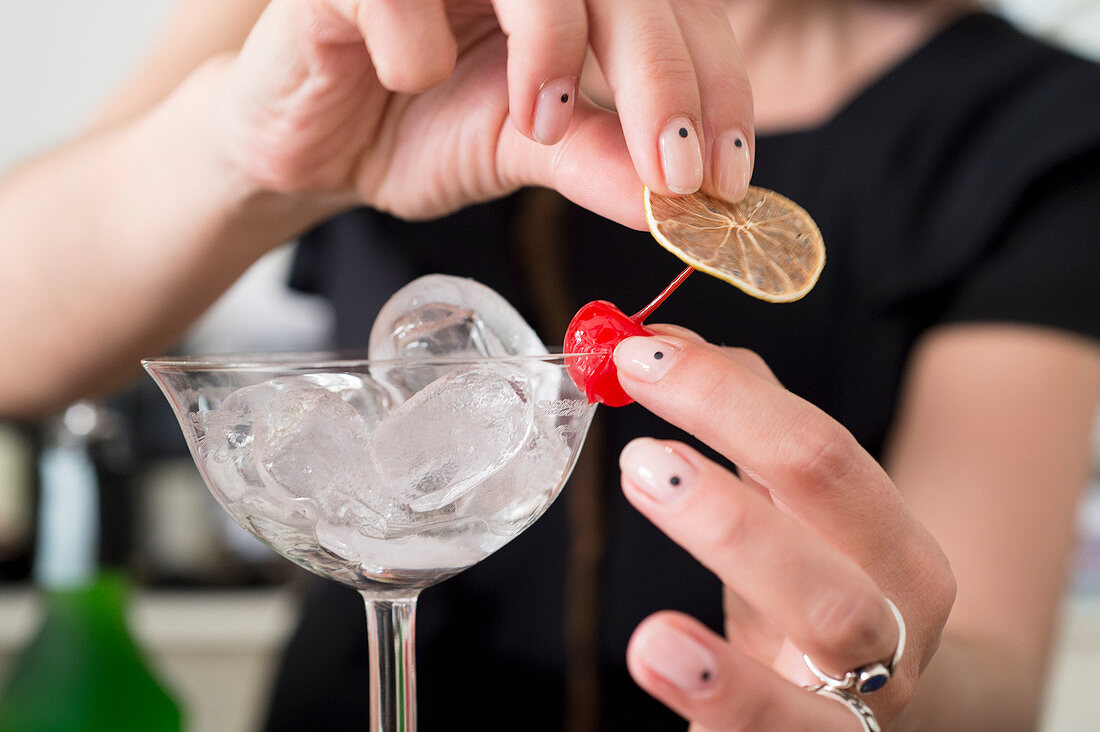 A cocktail glass being garnished with a cocktail cherry and a lime slice