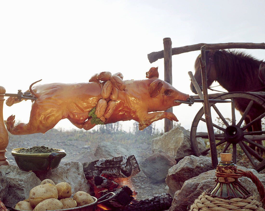A whole grilled suckling pig on a spit, sausages, a horse, boiled potatoes and wine