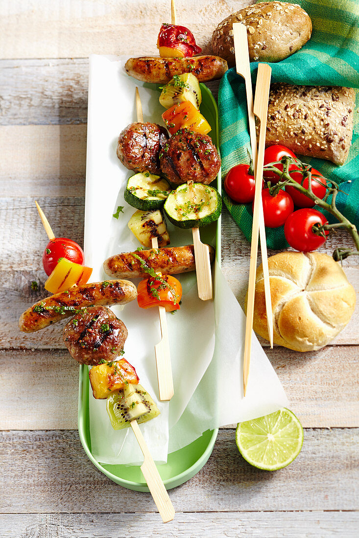 Grilled skewers with meatballs, sausages and vegetables from New Zealand with cherry tomatoes and bread rolls