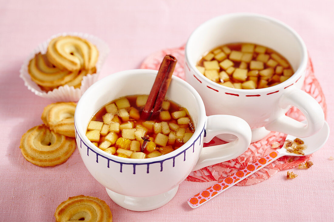 Two cups of hot drinks made with apples, cloves, tea, rock sugar, cinnamon and Calvados served with biscuits