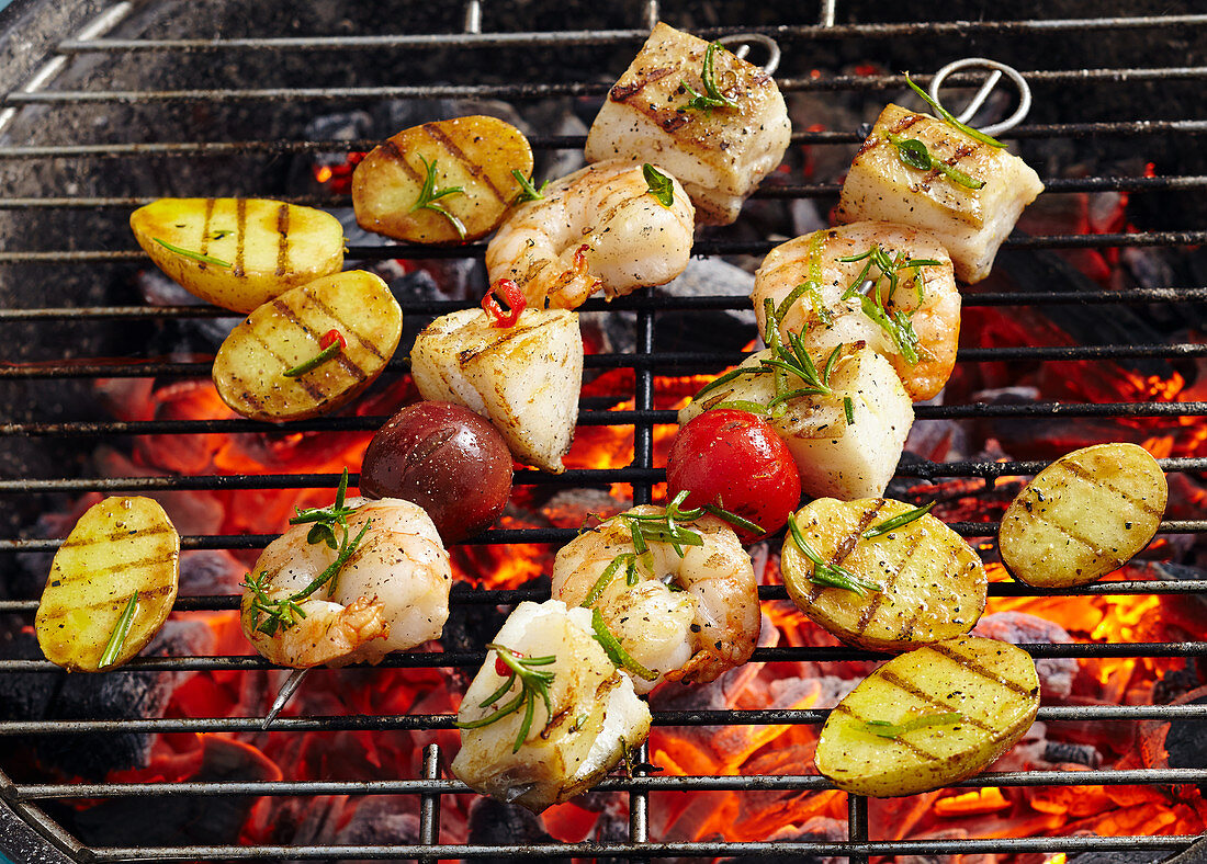 Cod and prawn skewers with grilled potatoes on a coal-fired grill