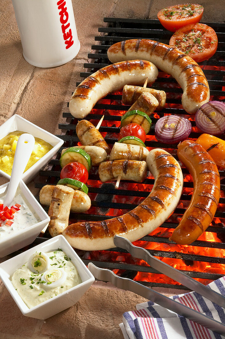 Sausages and sausage skewers on a grill with a trio of dips