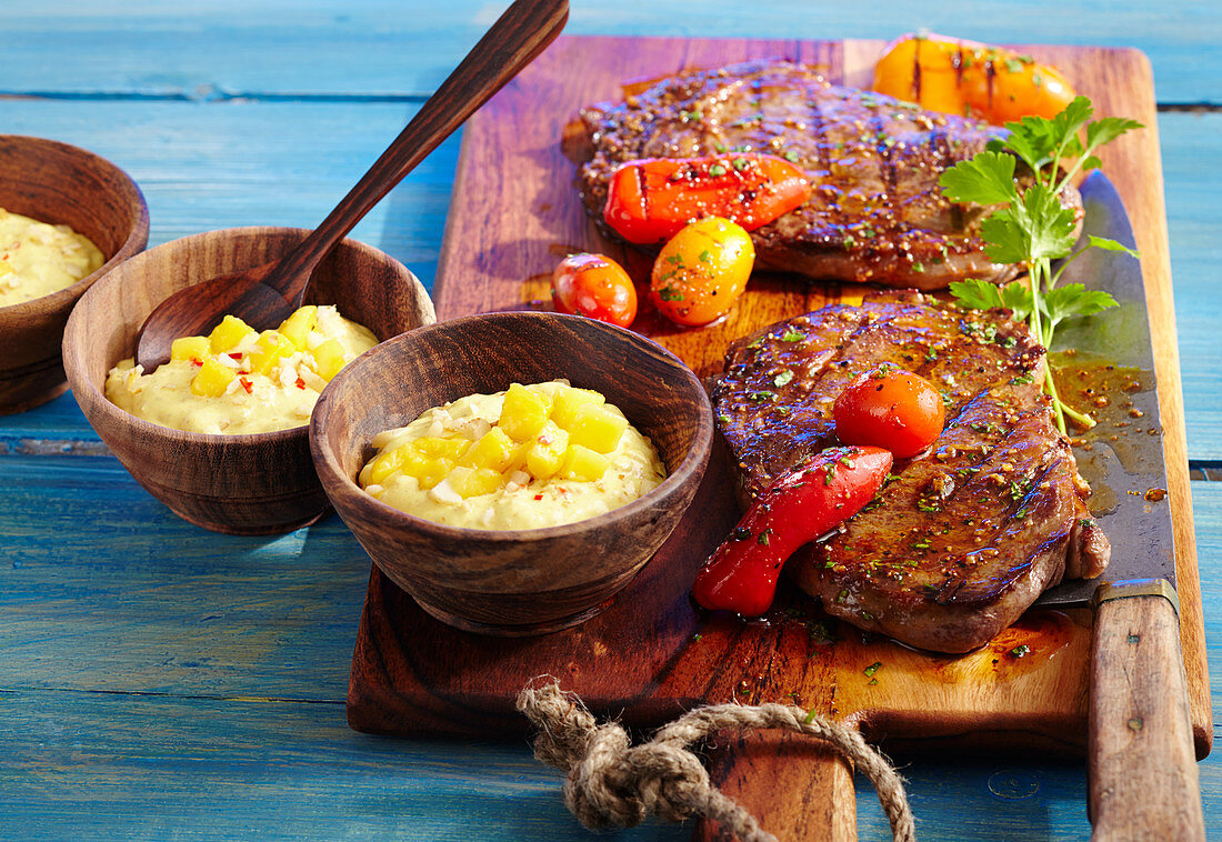 Two marinated, grilled club steaks with a mango dip, peppers and tomatoes