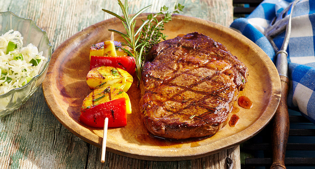 Marinated, grilled rib-eye steak with coleslaw and potato skewers on a wooden plate