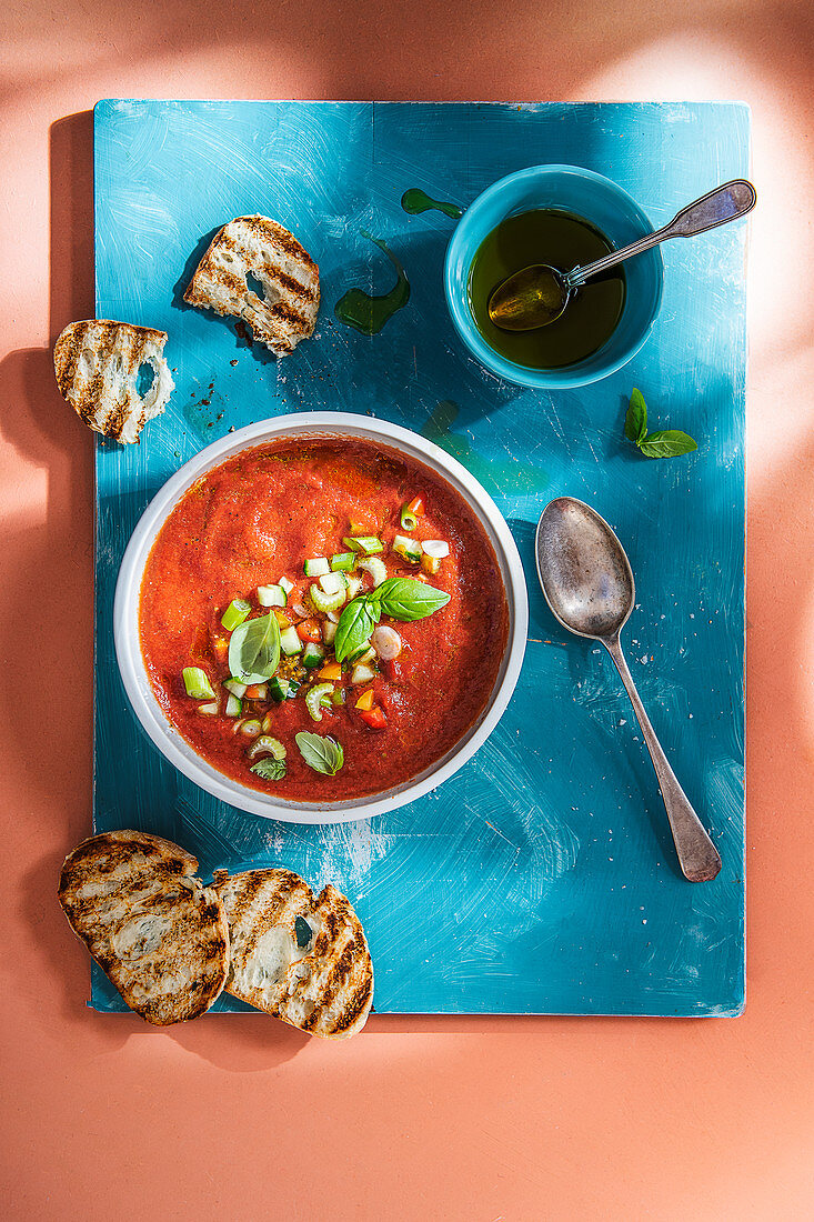 Cold gazpacho soup with basil and olive oil, bread on a side.