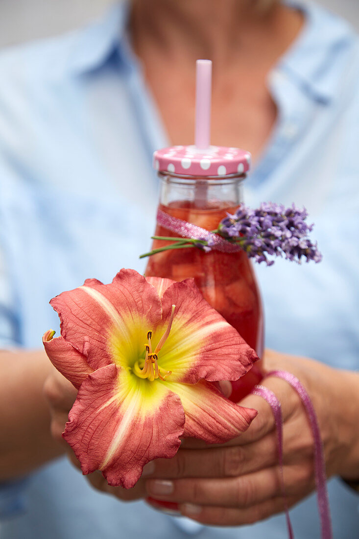 Hände halten Taglilien Blüte und Trinkflasche mit Lavendelsträußchen