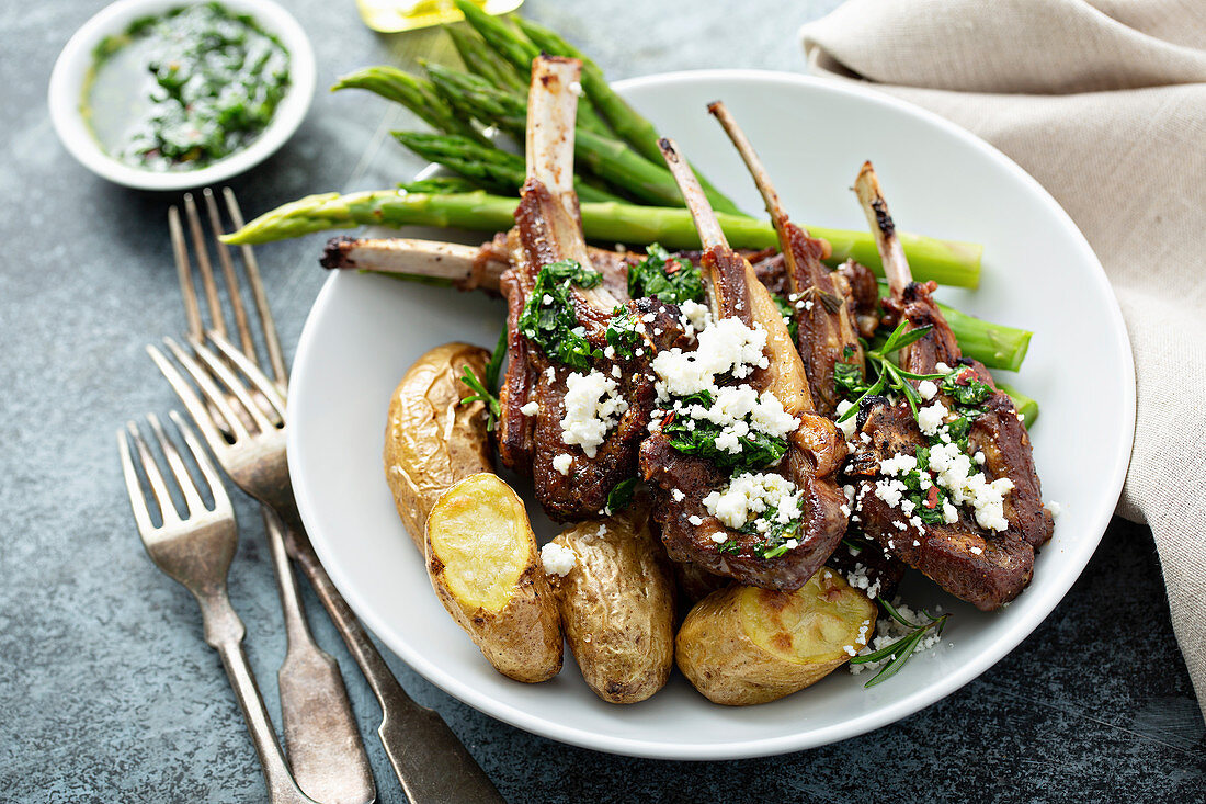 Grilled lamb chops with green herb sauce, feta, asparagus and potatoes served on a wooden board