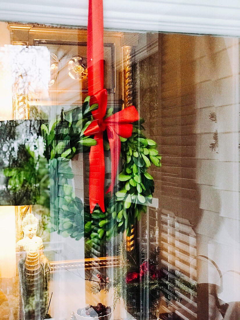 Festive wreath with red ribbon hung behind window
