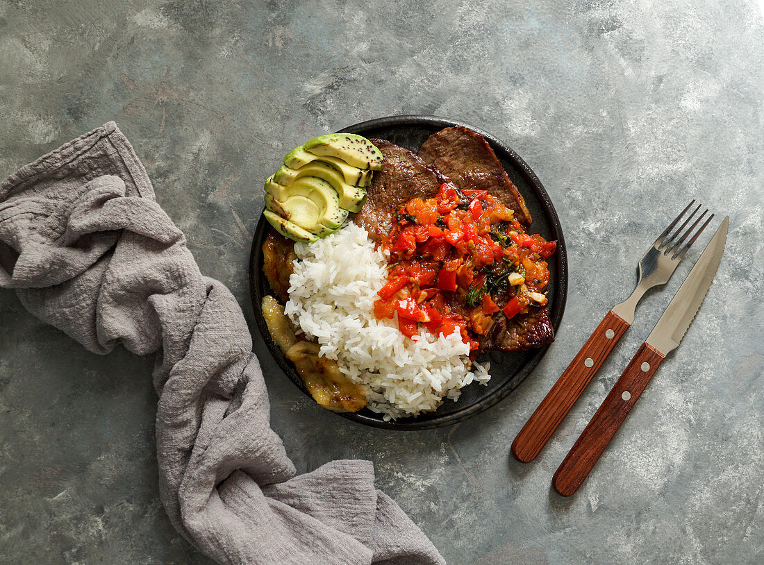 Bistec à la Criolla (Rindersteak mit Tomatensauce, Reis, Avocado, Bananenpommes, Kolumbien)