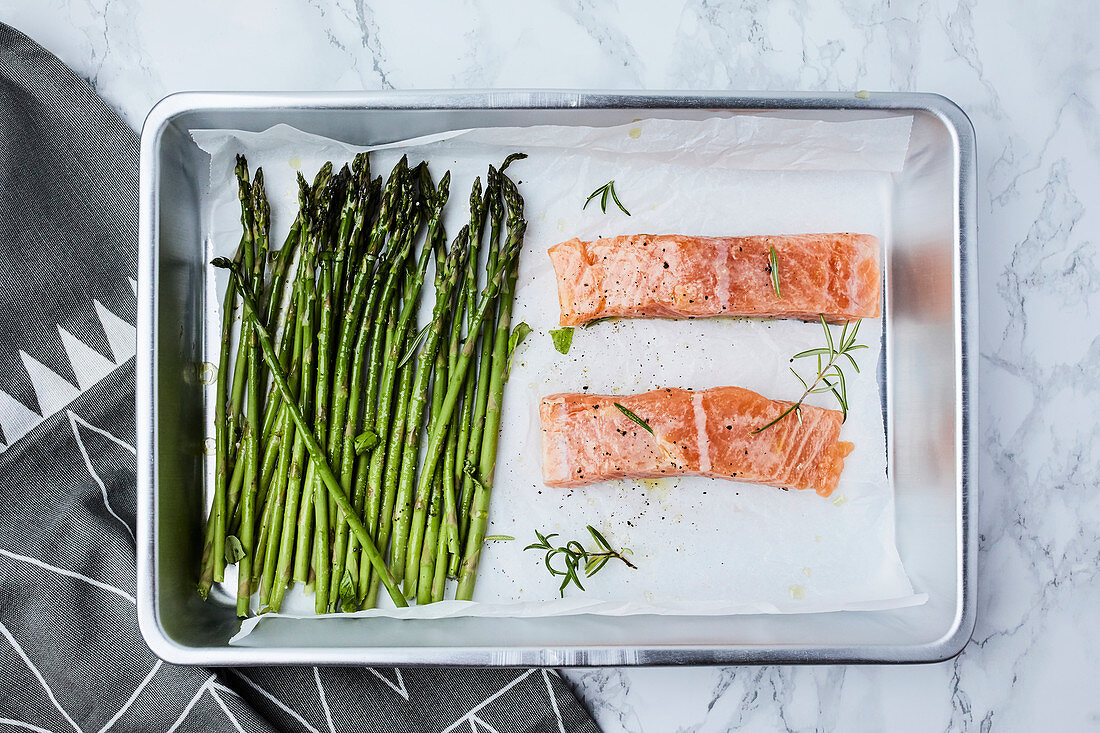 Salmon and asparagus in the pan, ready for oven, seasoned with olive oil and rosemary