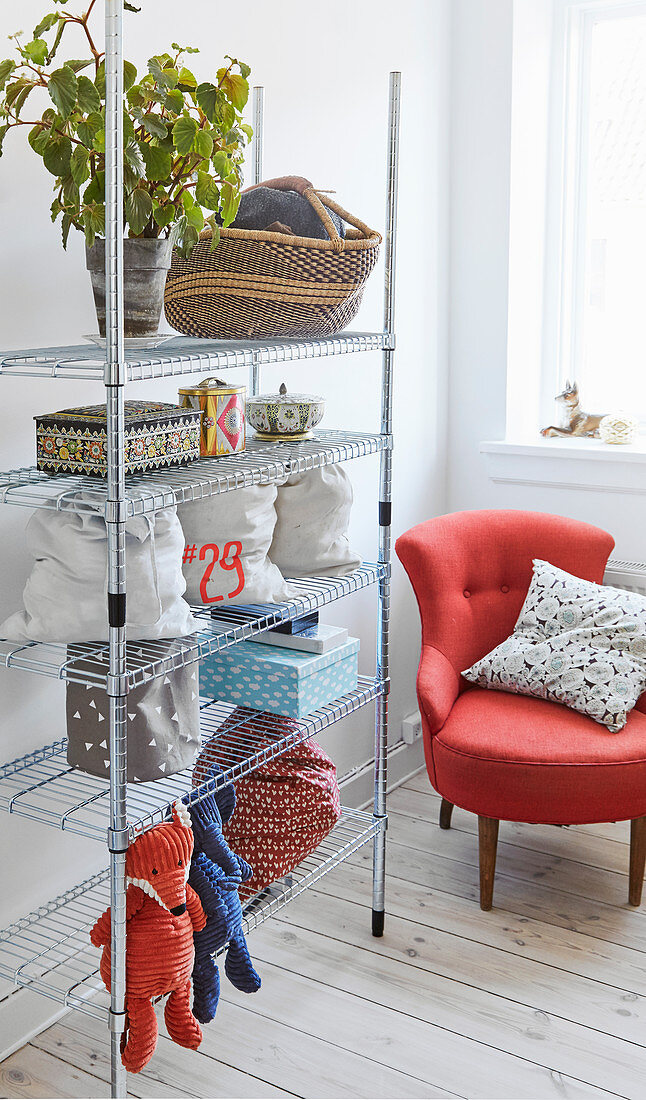 Modern metal shelves next to tomato-red armchair in corner