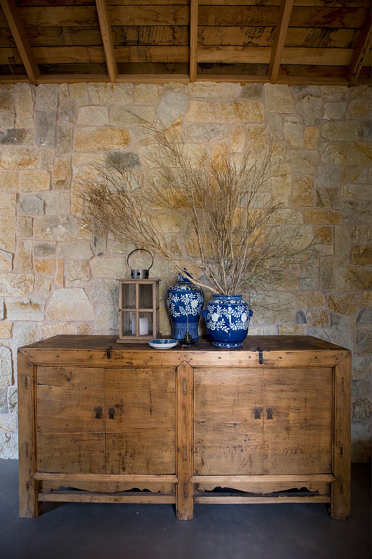 Blue-and-whit vases and lantern on rustic wooden cabinet against stone wall