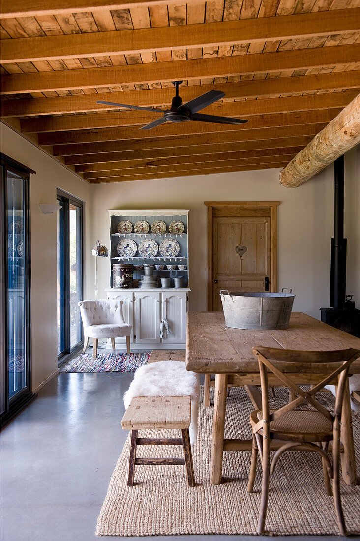 Rustic dining table with wooden bench and wooden chair with dresser in background