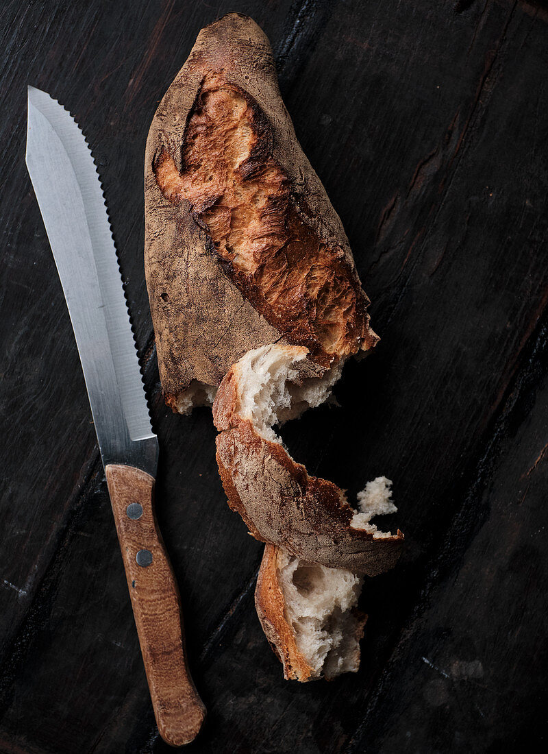 A loaf of crusty white bread and a breach knife on a black surface